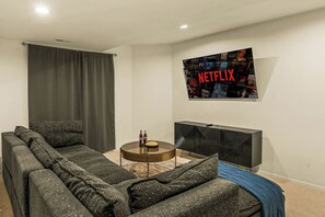 A living room with a sectional sofa, a coffee table, a flat-screen TV mounted on the wall, and a dark-colored entertainment unit.