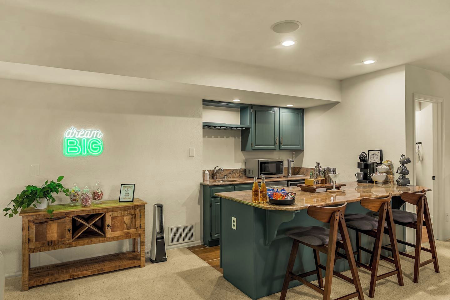 Een moderne keuken met blauwgroene kastjes, een neonbord en een bar met krukken.