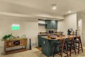 A modern kitchen with teal cabinets, a neon sign, and a bar area with stools.