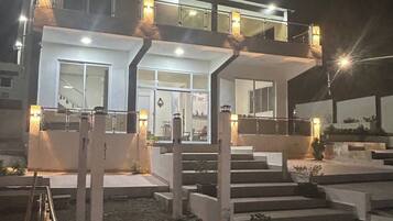 Un edificio moderno de dos pisos con balcón, ventanas amplias y una escalera que conduce a la entrada.