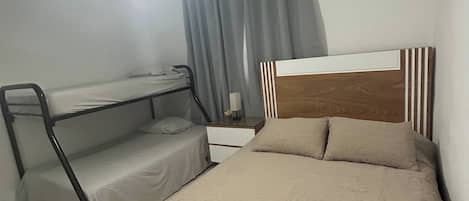 Un dormitorio con una cama individual doble, un escritorio, una cama con cabecera, un ventilador de techo y un equipo de aire acondicionado.