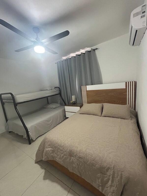 A bedroom with a bunk bed, a desk, a bed with a headboard, a ceiling fan, and an air conditioning unit.