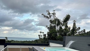 En tagterrasse med jacuzzi, barstole og havudsigt.
