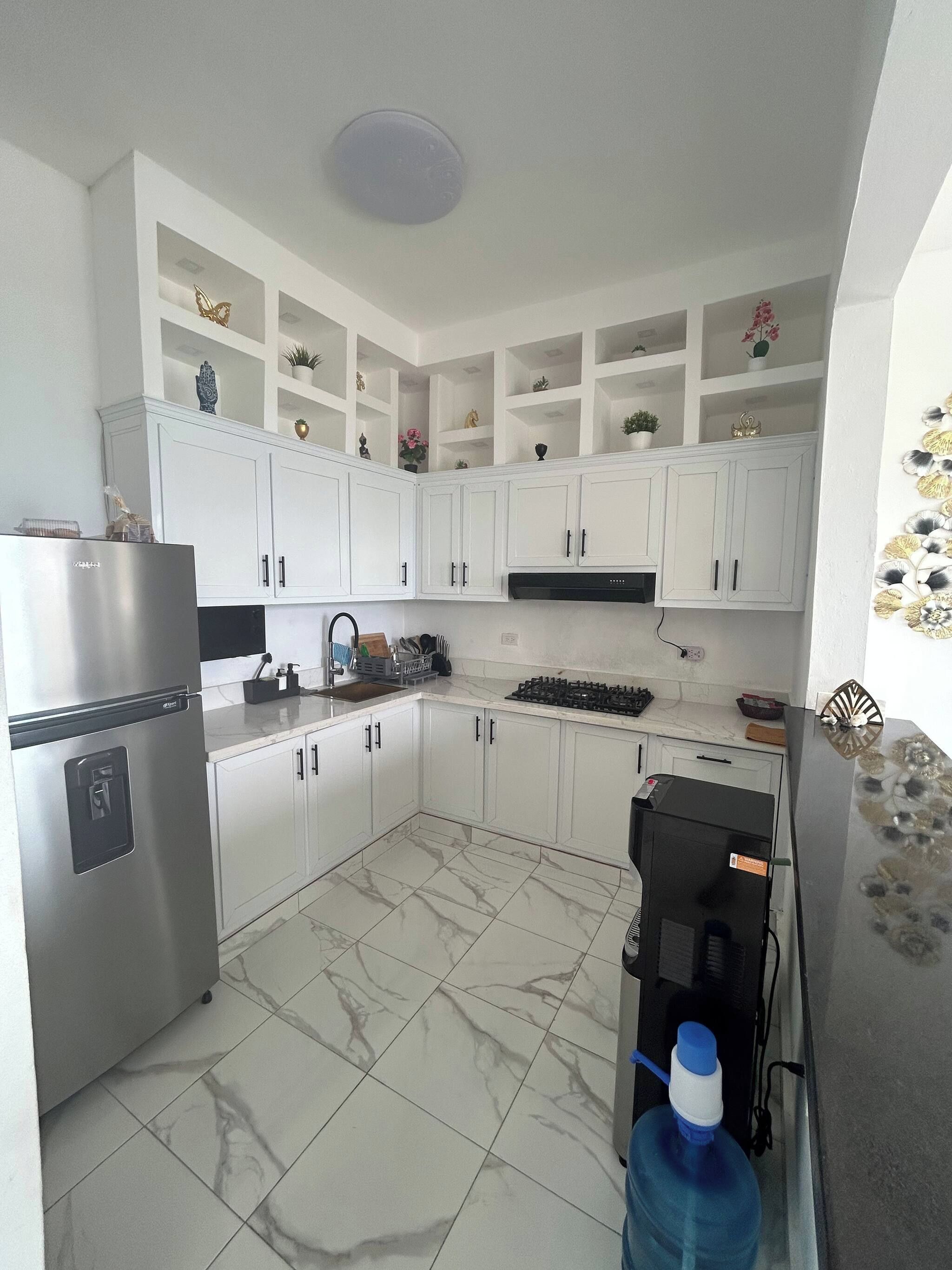 A kitchen with white cabinets, a stainless steel refrigerator, a gas stove, and a water dispenser.