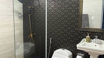 A bathroom with a glass shower enclosure, a toilet, and a sink with a mirror.