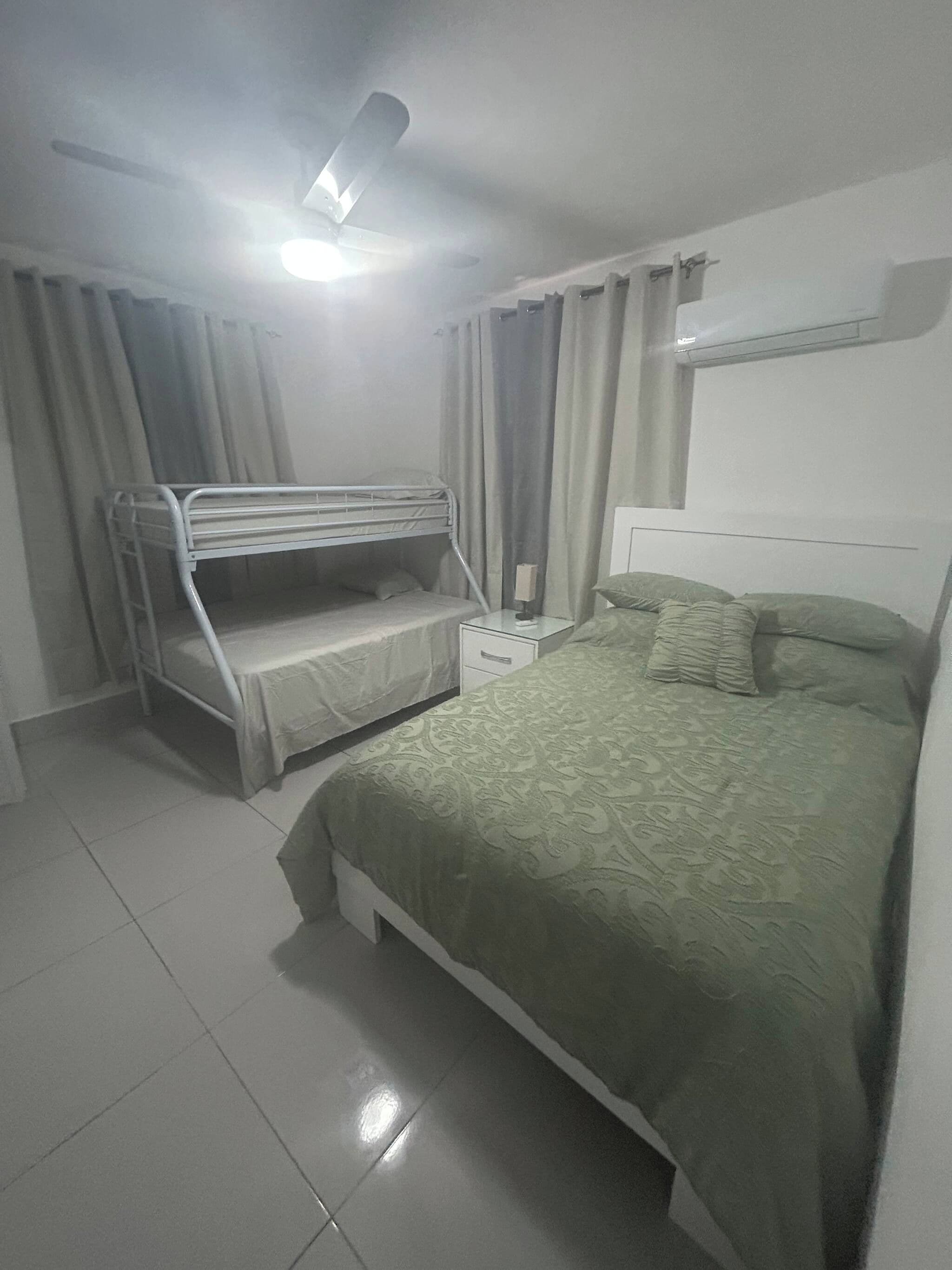 A bedroom with a bunk bed, a single bed, a nightstand, and a ceiling fan.