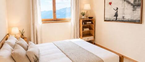 Una camera da letto con un letto di legno, una finestra con tende, una lampada da comodino, una luce a parete e un quadro incorniciato.