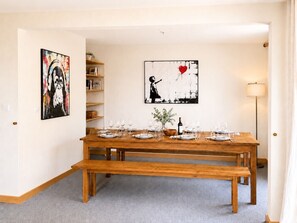 Ein Essbereich mit einem Holztisch, gedeckt für sechs Personen, flankiert von Bücherregalen und Kunstwerken.