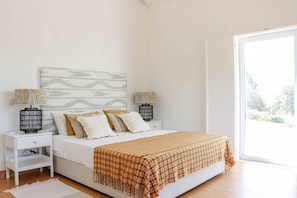 A bedroom with a bed, nightstands, lamps, a patterned throw blanket, and a large window.