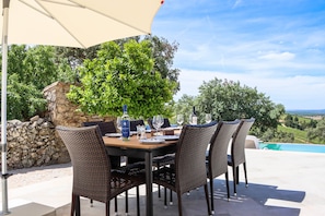 An outdoor dining area with a table set for four, surrounded by wicker chairs, under a canopy.