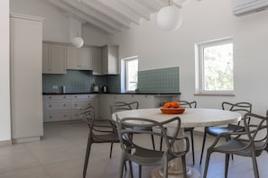 A modern kitchen with white cabinets, a round dining table, and a bowl of oranges.
