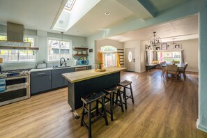 A spacious kitchen with a central island, wooden flooring, and a dining area with a table and chairs. - Treehouse - Sleeps 14, Hot Tub, 2-Story Solarium (Sioux Falls)
