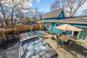 A backyard with a hot tub, outdoor furniture, a wooden deck, and a house with a blue exterior. - Treehouse - Sleeps 14, Hot Tub, 2-Story Solarium (Sioux Falls)
