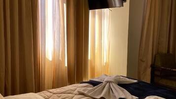 Habitación de hotel con cama, cortinas, televisor de pantalla plana montado en la pared y cama bien hecha con manta.