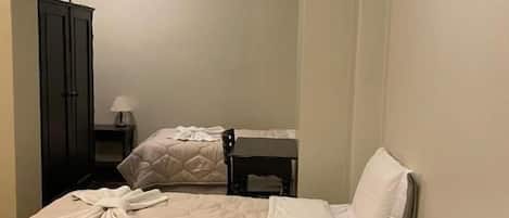 Quarto de hotel com duas camas, uma escrivaninha, uma cadeira, um abajur e ar condicionado.