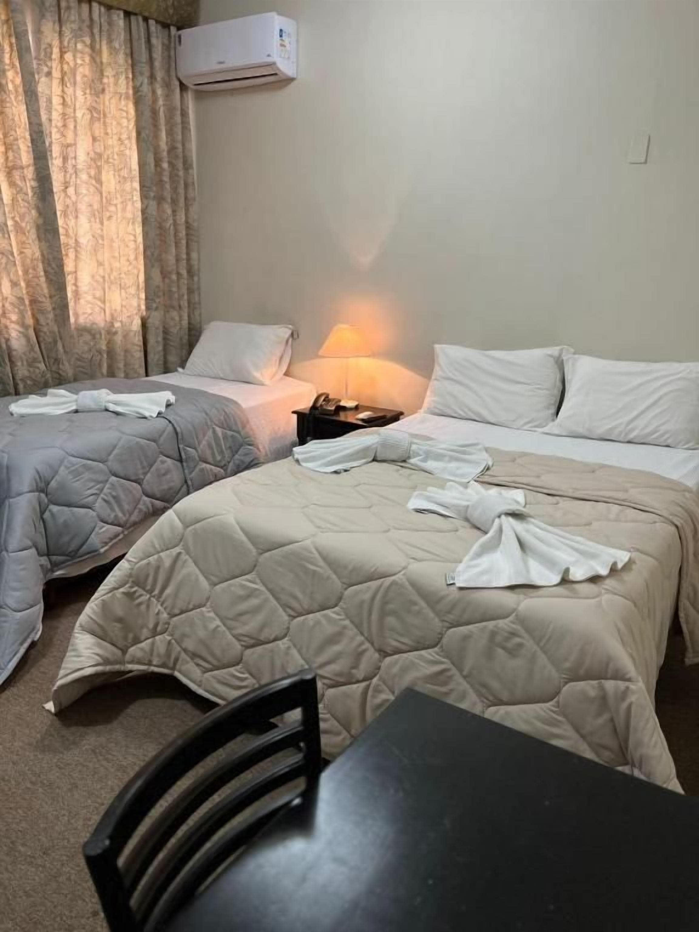 A hotel room with two beds, a table, and a chair.