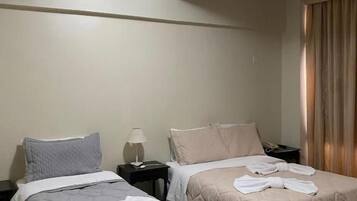 Hotellihuone, jossa on kaksi sänkyä, yöpöytä, lamppu ja kattovalaisin.
