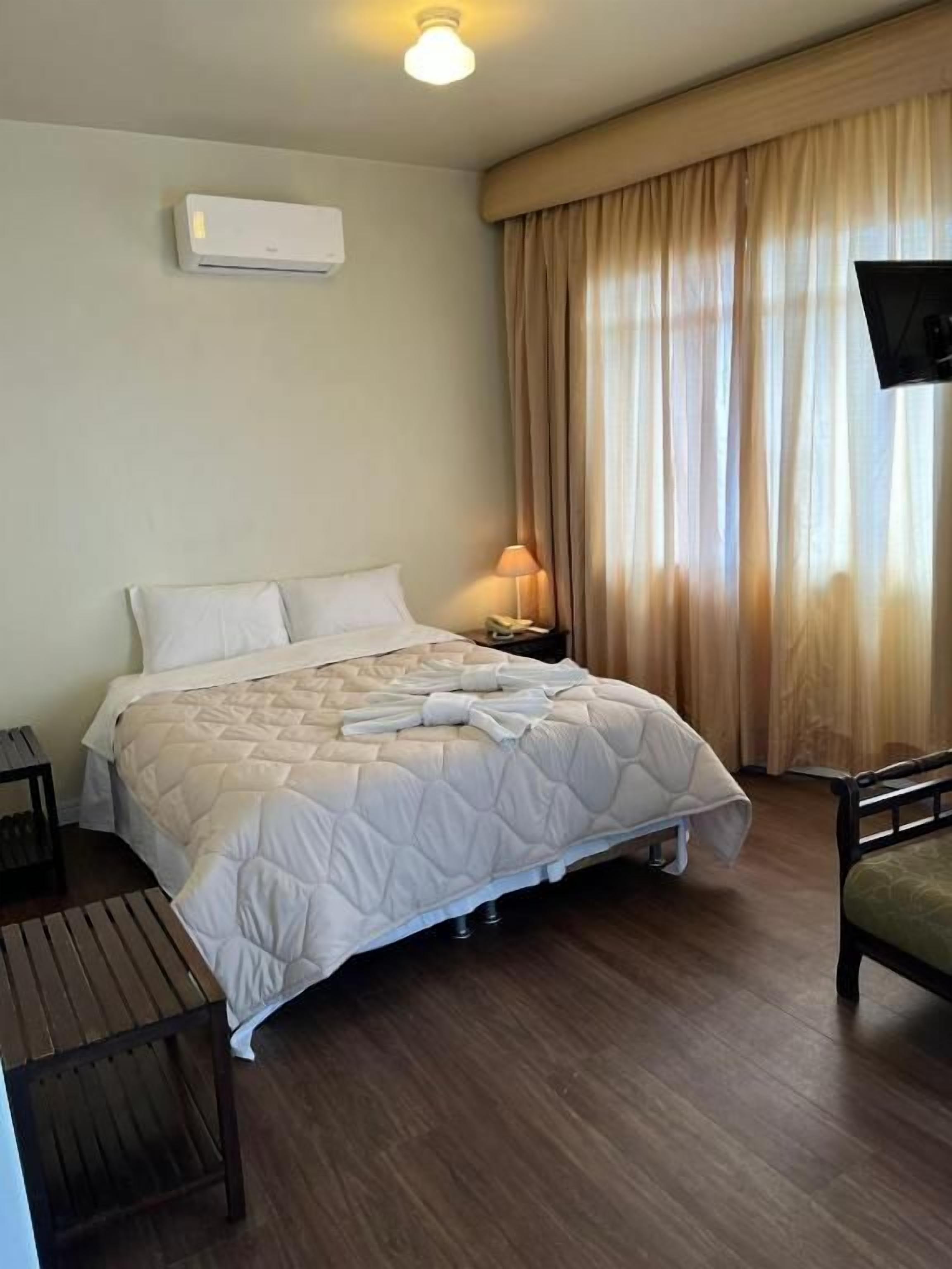 Una habitación de hotel con cama, mesita de noche, lámpara y televisor.