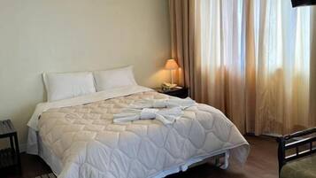 Una habitación de hotel con cama, mesita de noche, lámpara y televisor.