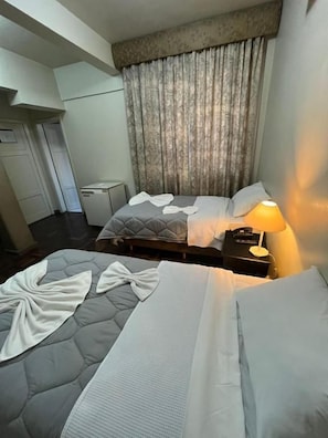 Et hotelværelse med to senge, et sengebord med en lampe og et lille skrivebord med en computer.
