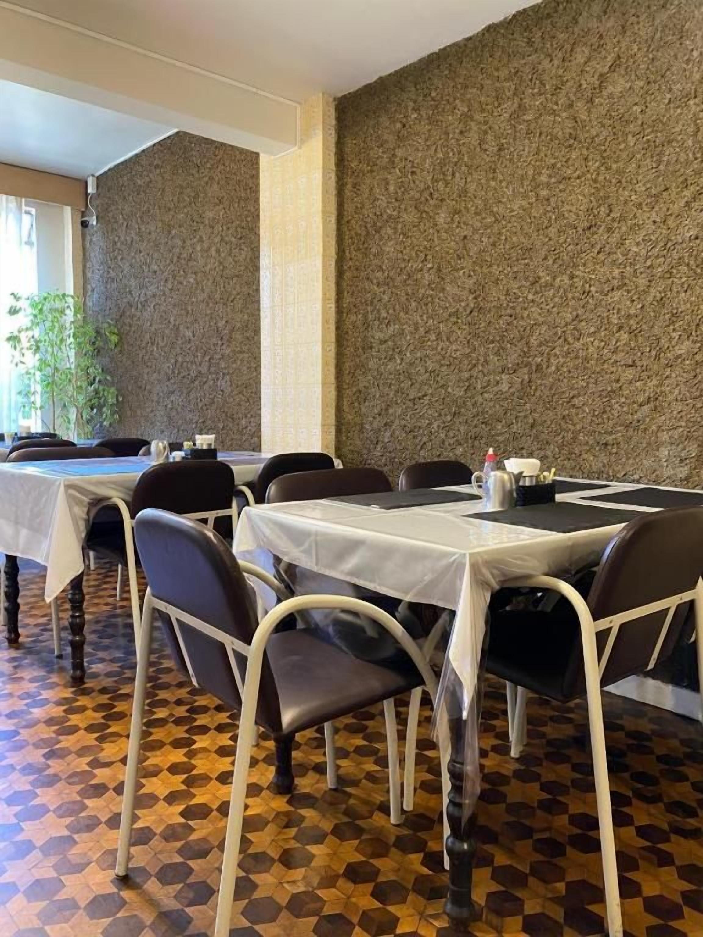 A restaurant interior with tables and chairs, a patterned floor, and a textured wall.