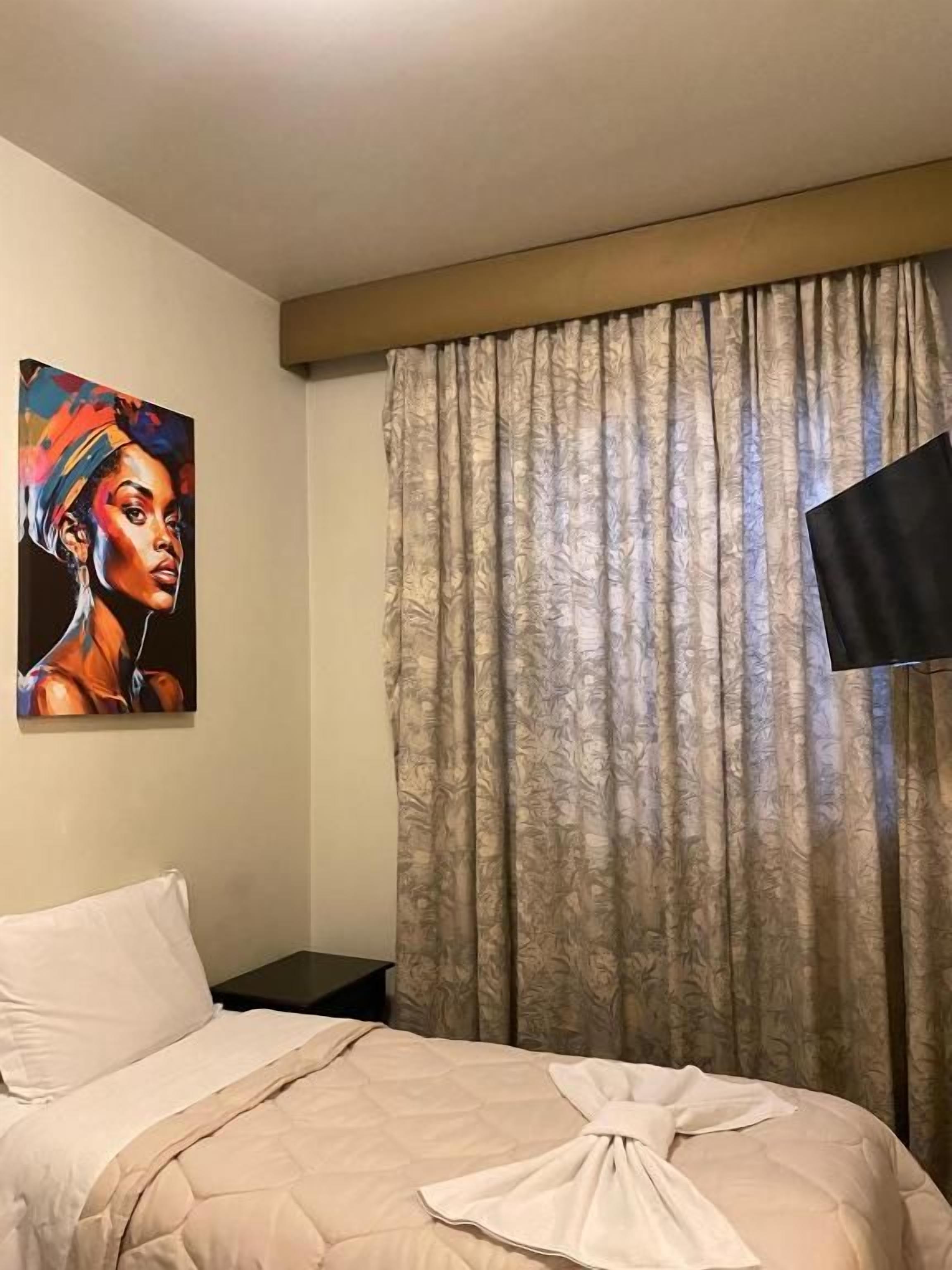 Una habitación de hotel con una cama, un cuadro en la pared y una ventana con cortinas.