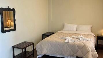 A bedroom with a bed, bedside tables, a nightstand, a chair, a mirror, and an air conditioning unit.
