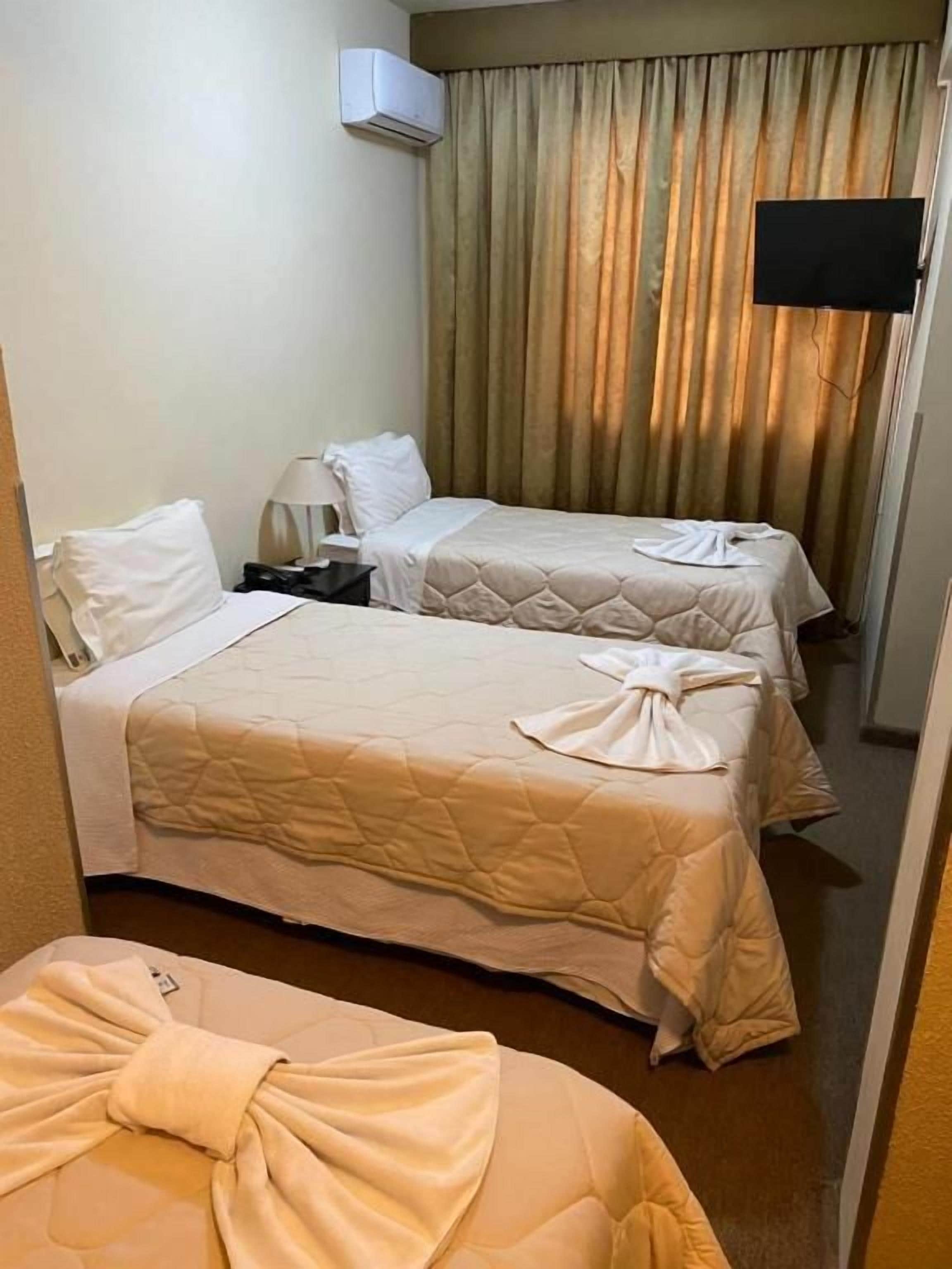 A hotel room with two beds, a flat-screen TV, and a window with curtains.
