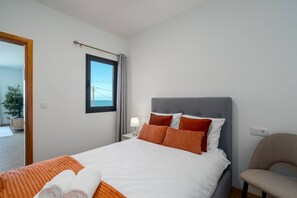 A hotel room with a bed, a chair, a nightstand, a lamp, a window with curtains, and a view of the sea. - Casa dos Pescadores by Galmi (Calheta (Madeira))