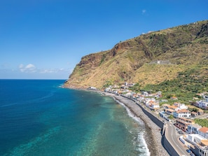 A coastal town with buildings along the shoreline, a clear blue sea, and a hillside with vegetation. - Casa dos Pescadores by Galmi (Calheta (Madeira))