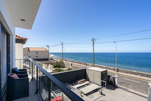 A balcony with a view of the sea, a building with a tiled roof, and a street with parked cars. - Casa dos Pescadores by Galmi (Calheta (Madeira))