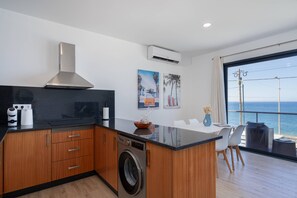 Una cocina moderna con lavadora incorporada, armarios de madera y un amplio ventanal con vista al mar.