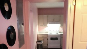 A hallway with pink walls, a wooden floor, and a kitchen area with white cabinets and a stove. - 2-bedroom home great for workforce housing, family, and content creation! (Americus)