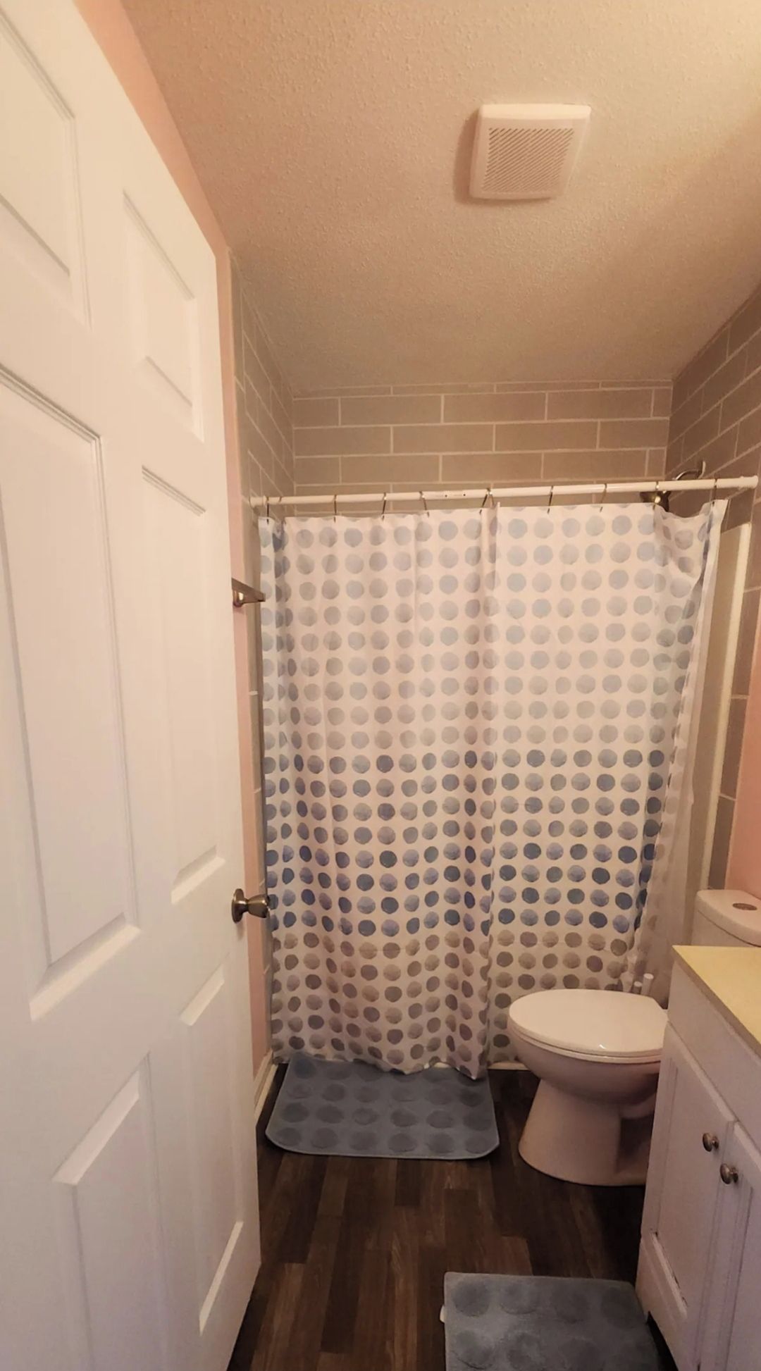 A bathroom with a white door, a shower curtain with a polka dot pattern, a toilet, and a small rug on the floor.