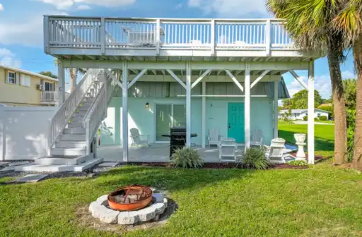 A two-story house with a balcony, a staircase, and a fire pit in the yard.