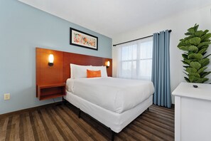 A hotel room with a bed, two bedside tables, a nightstand, a window with curtains, and a wall-mounted picture. - Tranquil 2Bed/2Bath with Balcony Near Universal (Orlando)