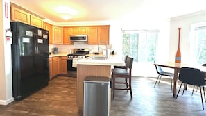 A kitchen with wooden cabinets, a black refrigerator, a microwave, and a stove. There is a small island with a sink and chairs.
