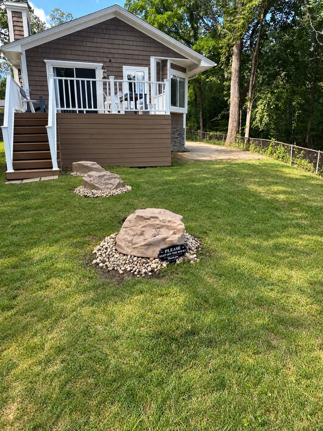 A house with a front porch, a stone pathway, and a sign that says 'PLEASE KEEP OFF THE ROCKS.'