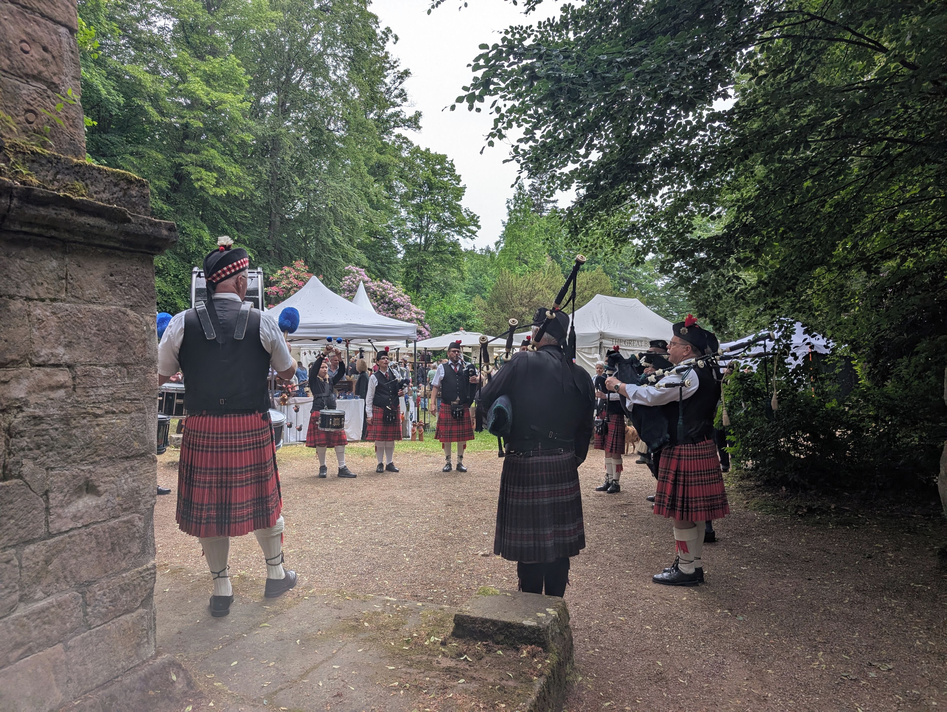 Een groep mensen in traditionele Schotse kledij, waaronder kilts en doedelzakken, verzameld buiten.