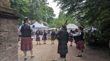 Een groep mensen in traditionele Schotse kledij, waaronder kilts en doedelzakken, verzameld buiten.