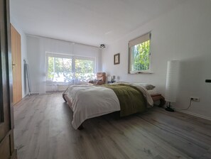 A bedroom with a large bed, a chair, a window, and a radiator. - La Maison sur la Colline – Eco-Friendly Getaway with Garden & Scenic Views (Höchst im Odenwald)