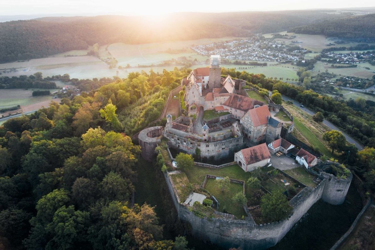 An aerial view of a historic castle surrounded by forested areas and a river.