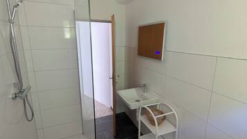 Ein Badezimmer mit einer Duschkabine, einem weißen Waschbecken, einem Spiegel und einem Regal mit einem Korb.