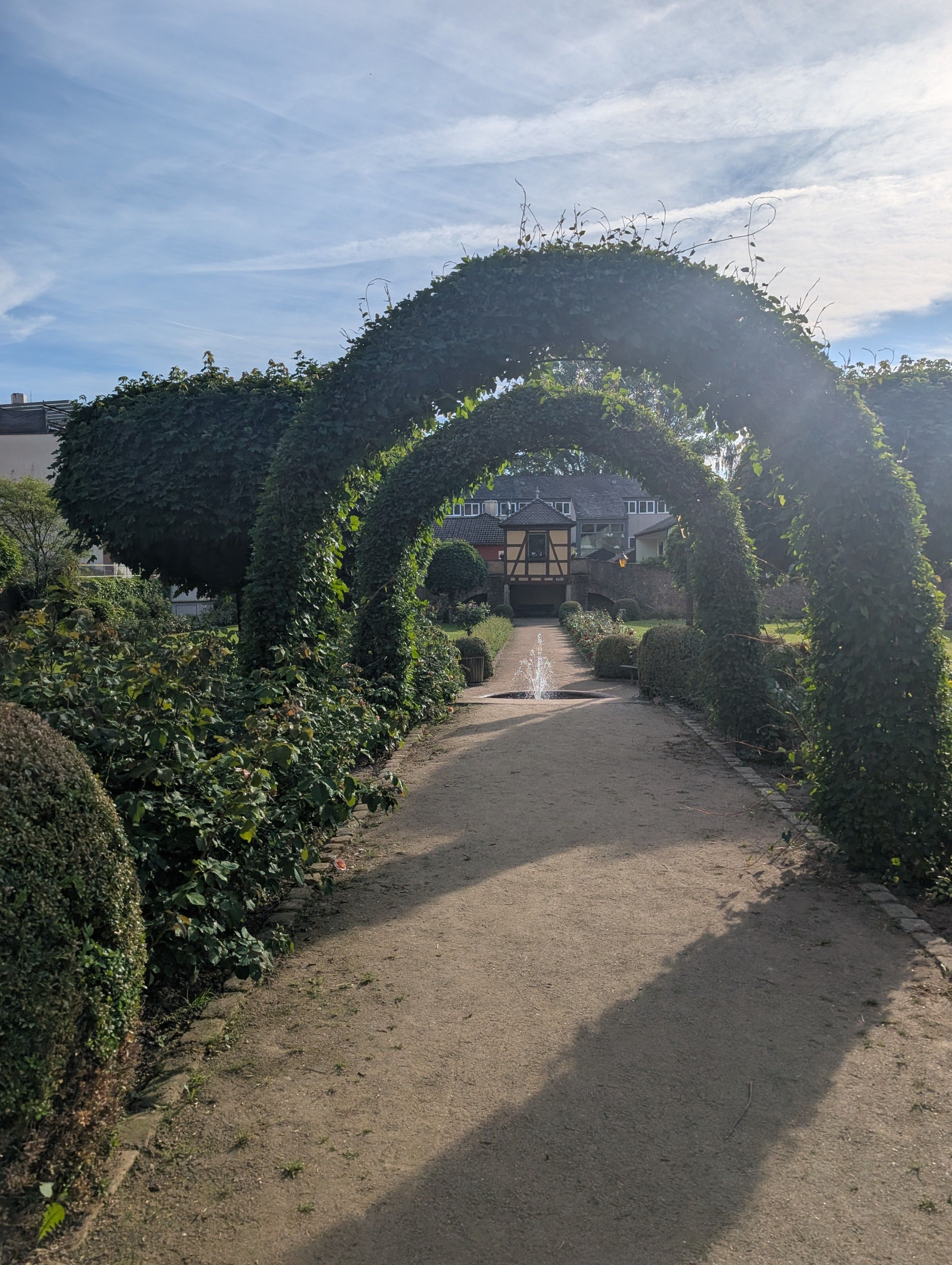 Ein Weg, der von ordentlich geschnittenen Hecken gesäumt wird, mit einem Gebäude im Hintergrund.