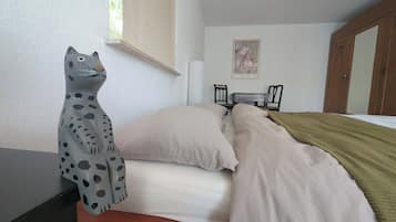A bedroom with a bed, a nightstand, a desk, a chair, and a window.