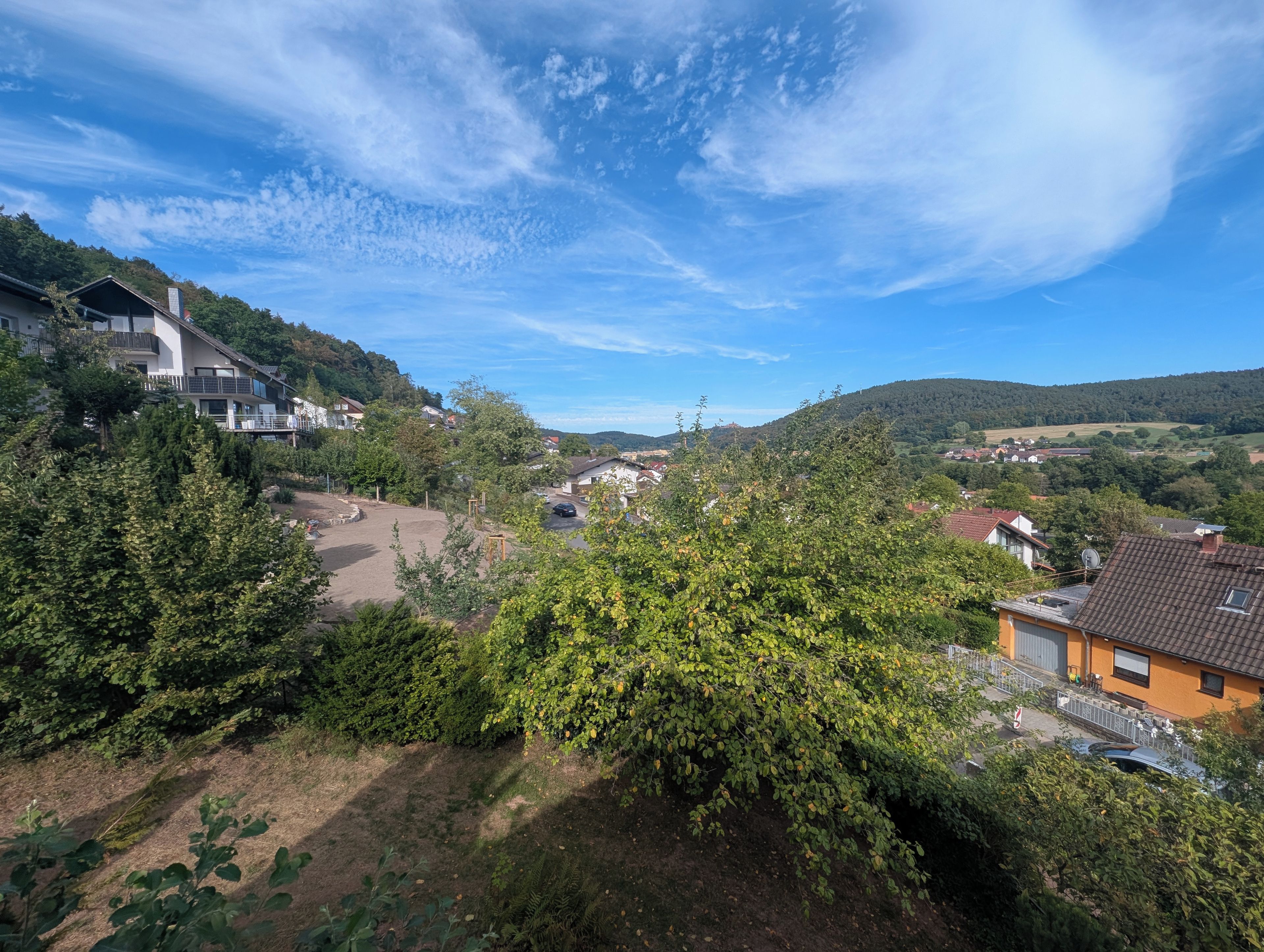 Ein Wohngebiet mit Häusern, blauem Himmel und hügeliger Landschaft im Hintergrund.