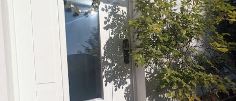 Una puerta blanca con un ventanal, un escalón que lleva a ella, y un muro de ladrillo a la derecha.