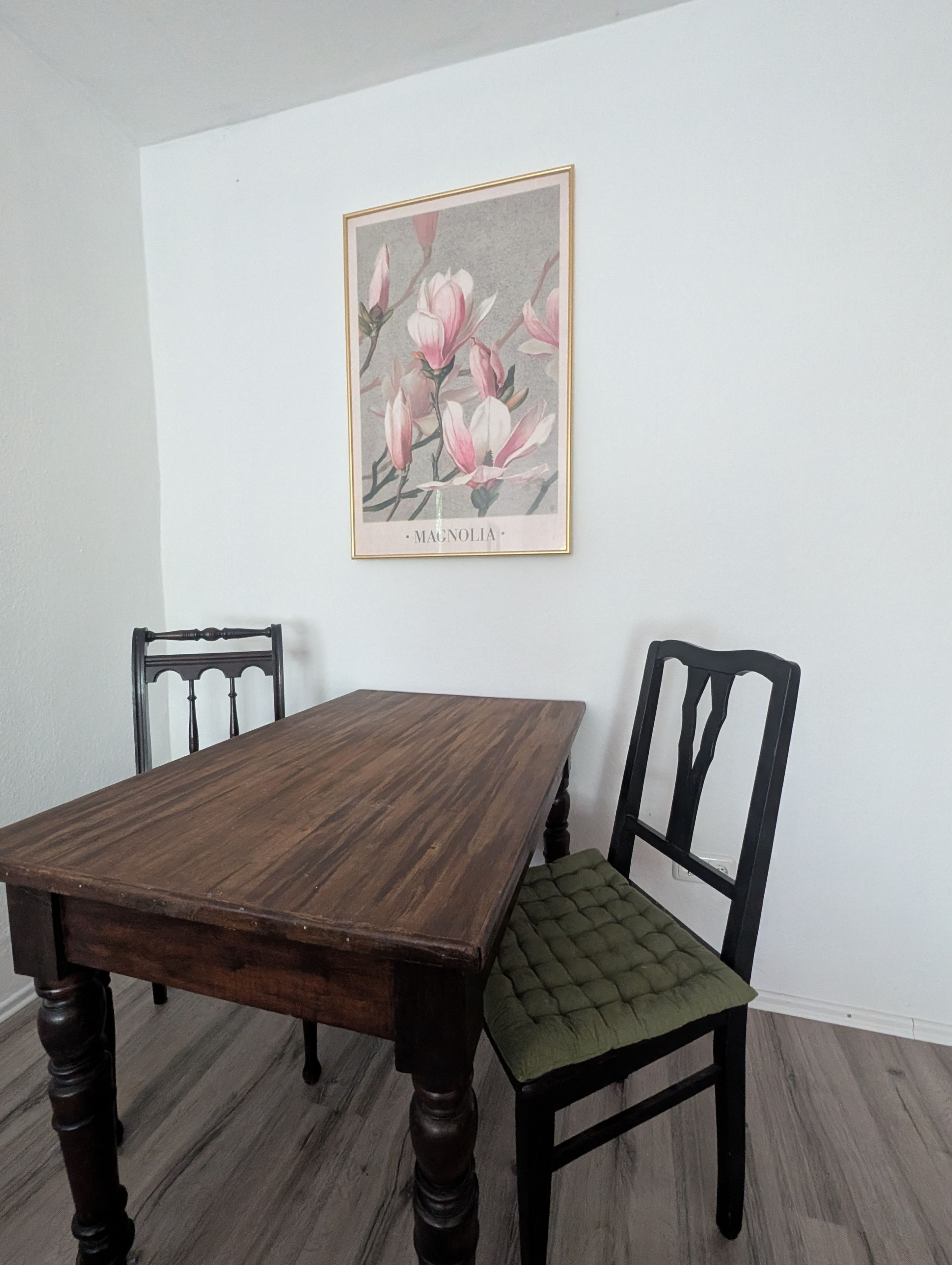 Une table à manger avec des chaises, une estampe botanique encadrée au mur et un plancher en bois.