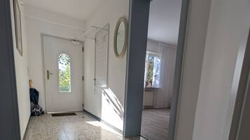 A hallway with a tiled floor, a door with a window, and a mirror on the wall.
