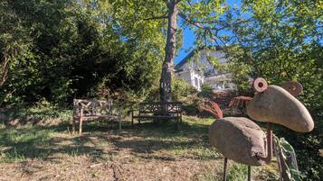 A garden with two wooden benches, a large rock sculpture, and a tree.
